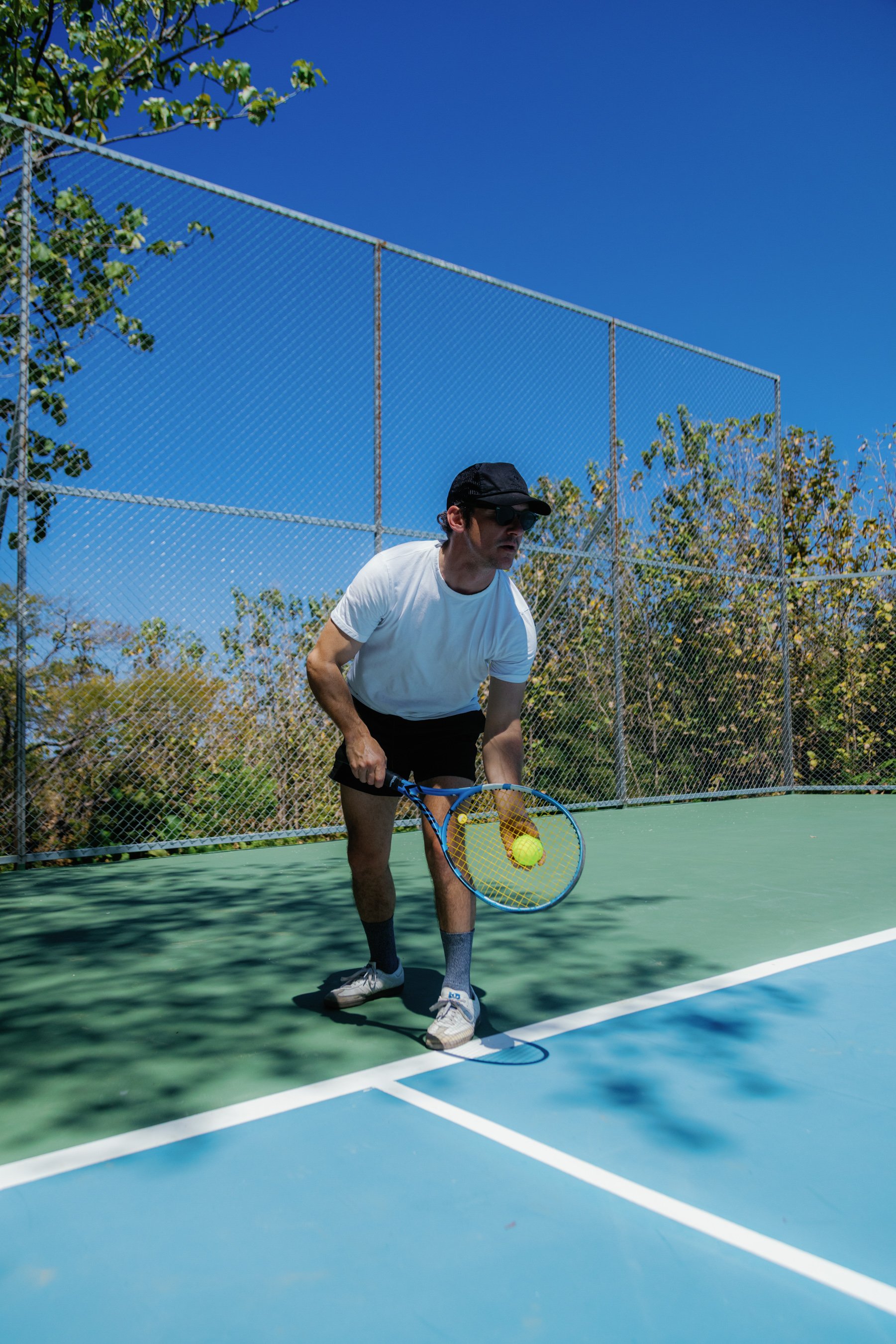 A man is playing tennis outdoors on a green and blue court. Outdoor pickleball and tennis courts at Solindo Stays in Marbella, Guanacaste, Costa Rica.