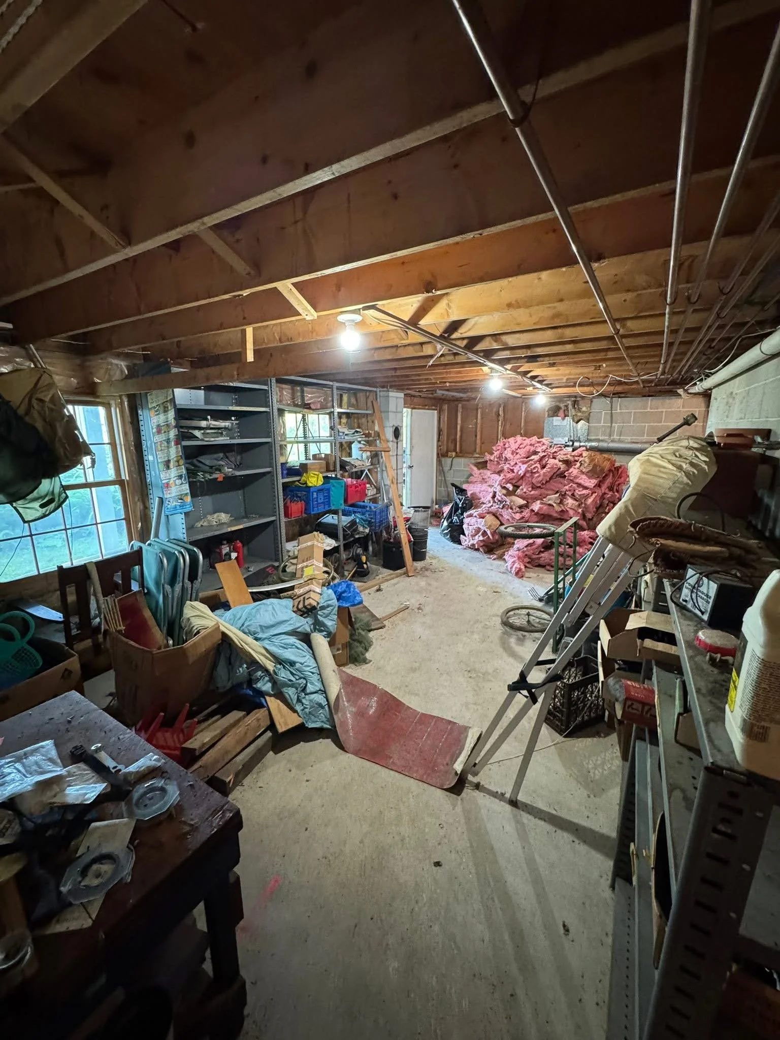 A cluttered garage with shelving units, a ladder, and loose insulation piled against the wall.
