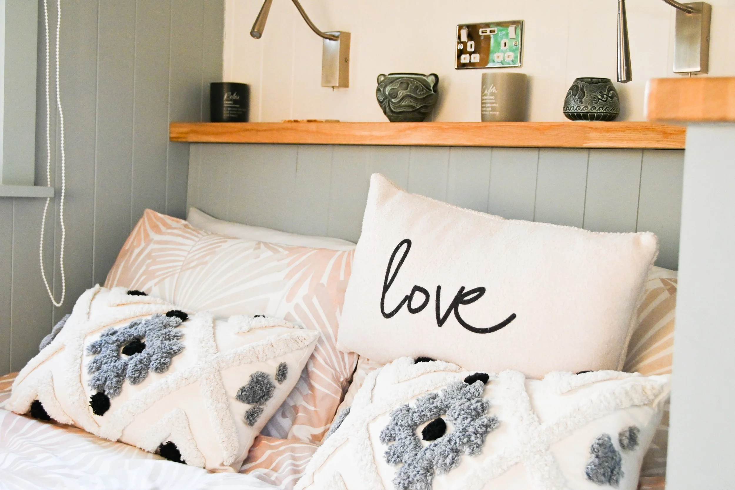 Decorative bed with pillows, including one with the word love, and a headboard shelf with vases and artwork.