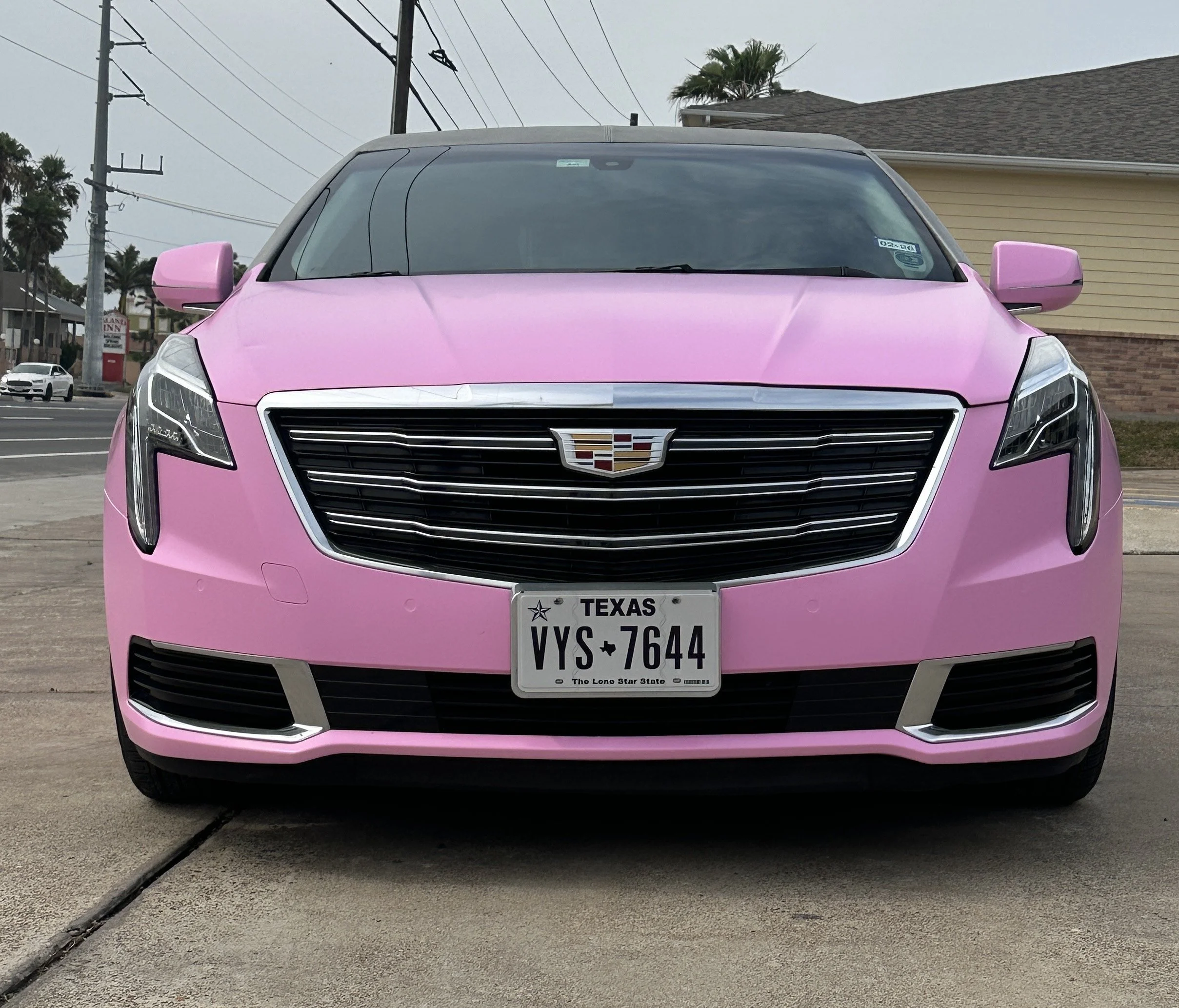 Front view of a pink Cadillac with Texas license plate VYS-7644 parked on concrete pavement.