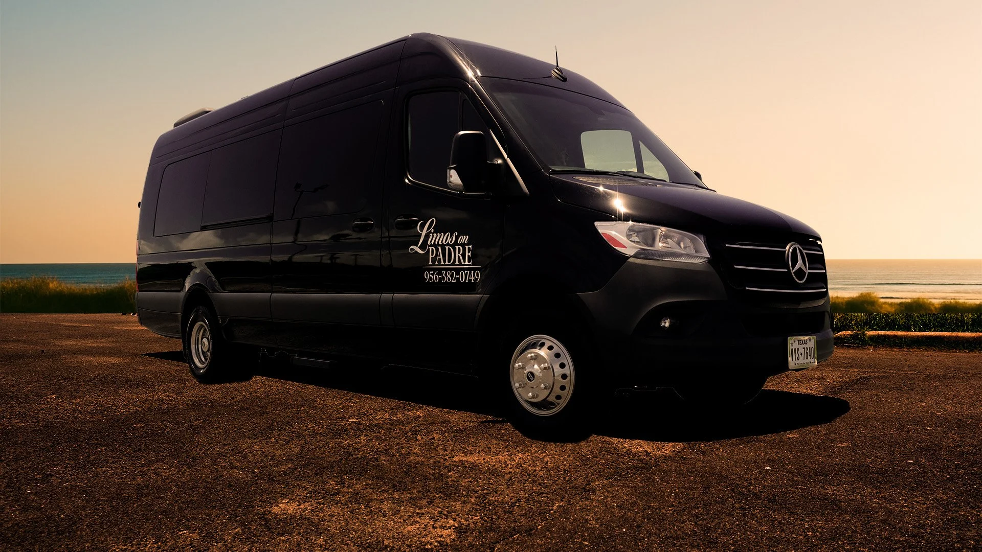 A black Mercedes-Benz sprinter van parked on a gravel surface near a beach during sunset, with contact information and company name 'Limos en PADRE' on the side.