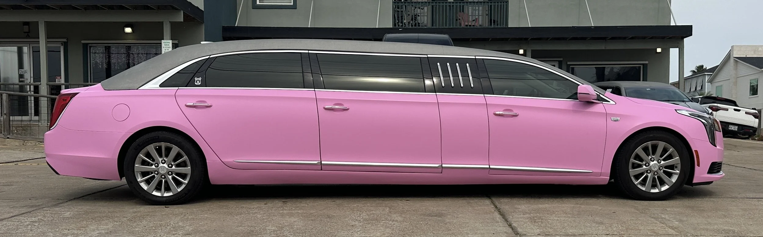 A pink limousine parked outside a building on a concrete surface.
