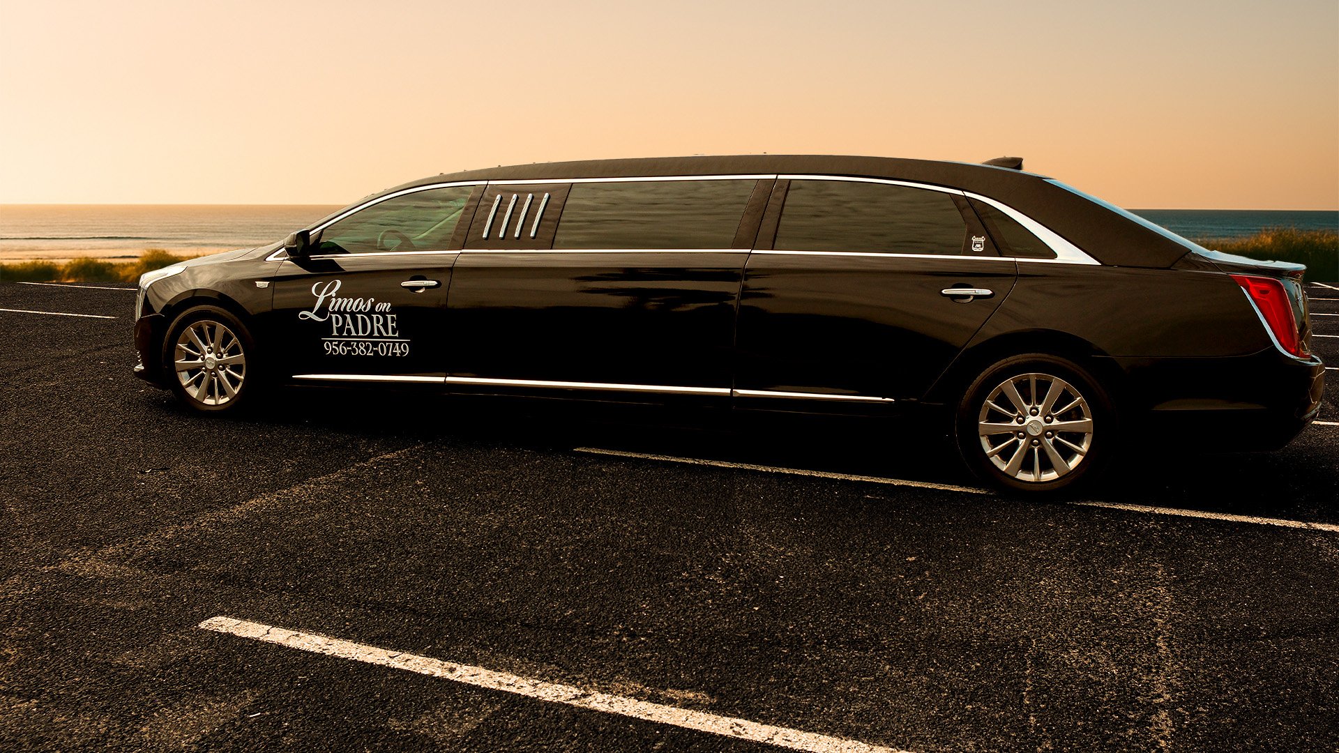 A black limousine parked on a parking lot near the beach at sunset, with the words "Limos on PADRE" and a phone number written on the side.