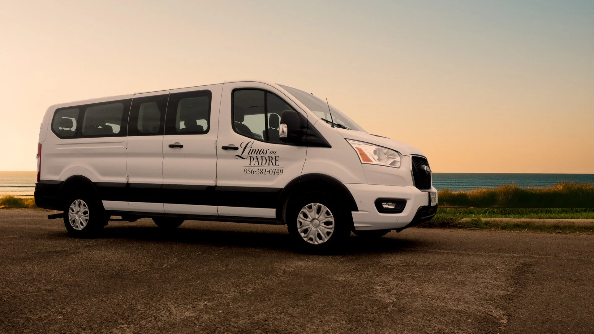 front view of a white passenger van parked near the beach at sunset with an ocean background