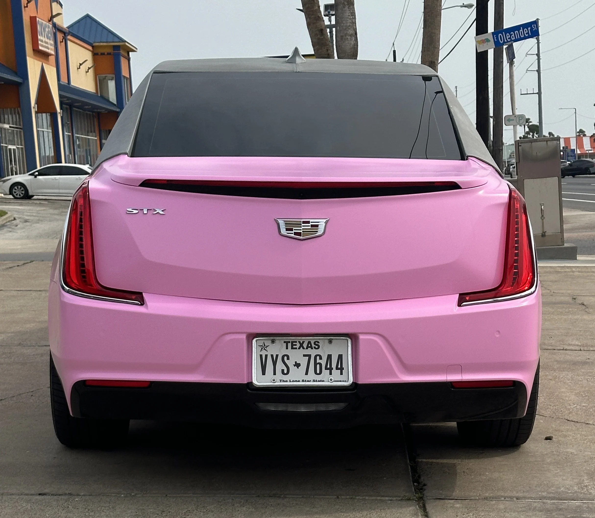 Rear view of a pink Cadillac STX with Texas license plate VYS 7644, parked on concrete pavement.