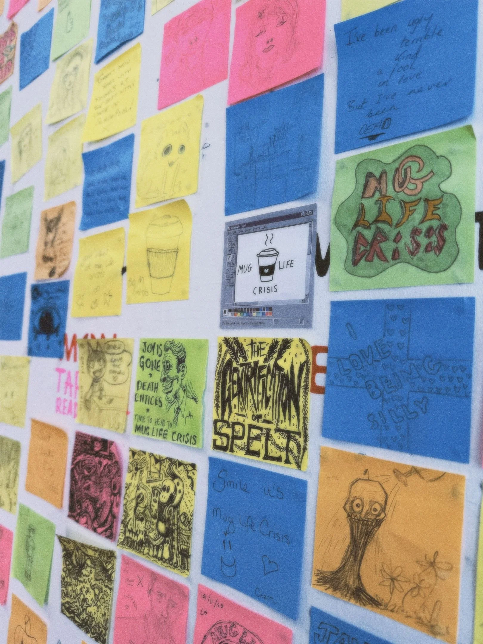 A wall with colorful sticky notes and drawings, including sketches of faces, abstract art, and messages like "MUG LIFE CRISIS" and "COMPLETION OF SPEED."