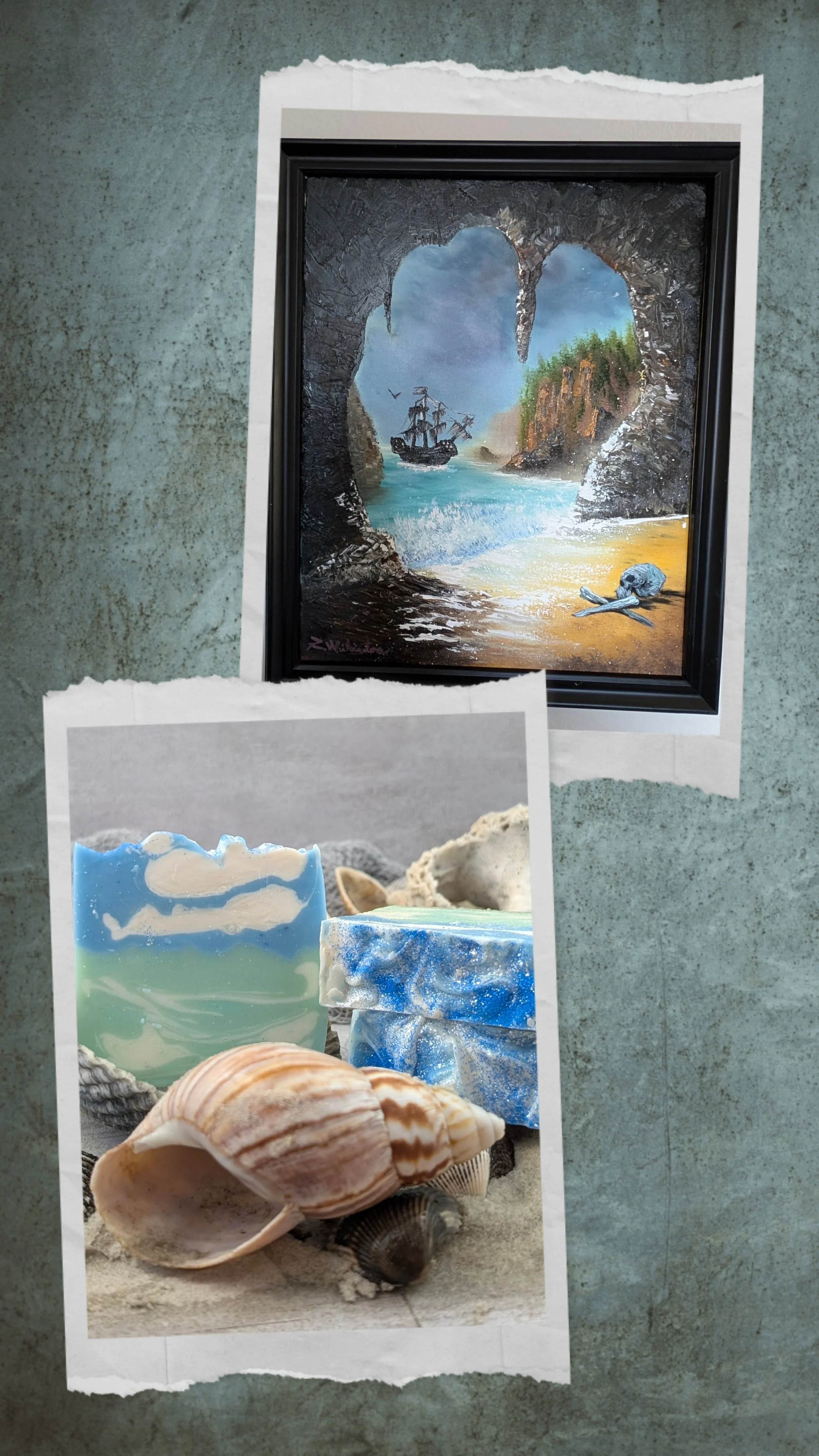 A framed painting of a pirate ship sailing through a sea cave opening onto a beach, with cliffs and green foliage in the background, and a skull and bones on the sand in the foreground. Below, there are seashells and soap bars with ocean and beach designs in front of a gray background.