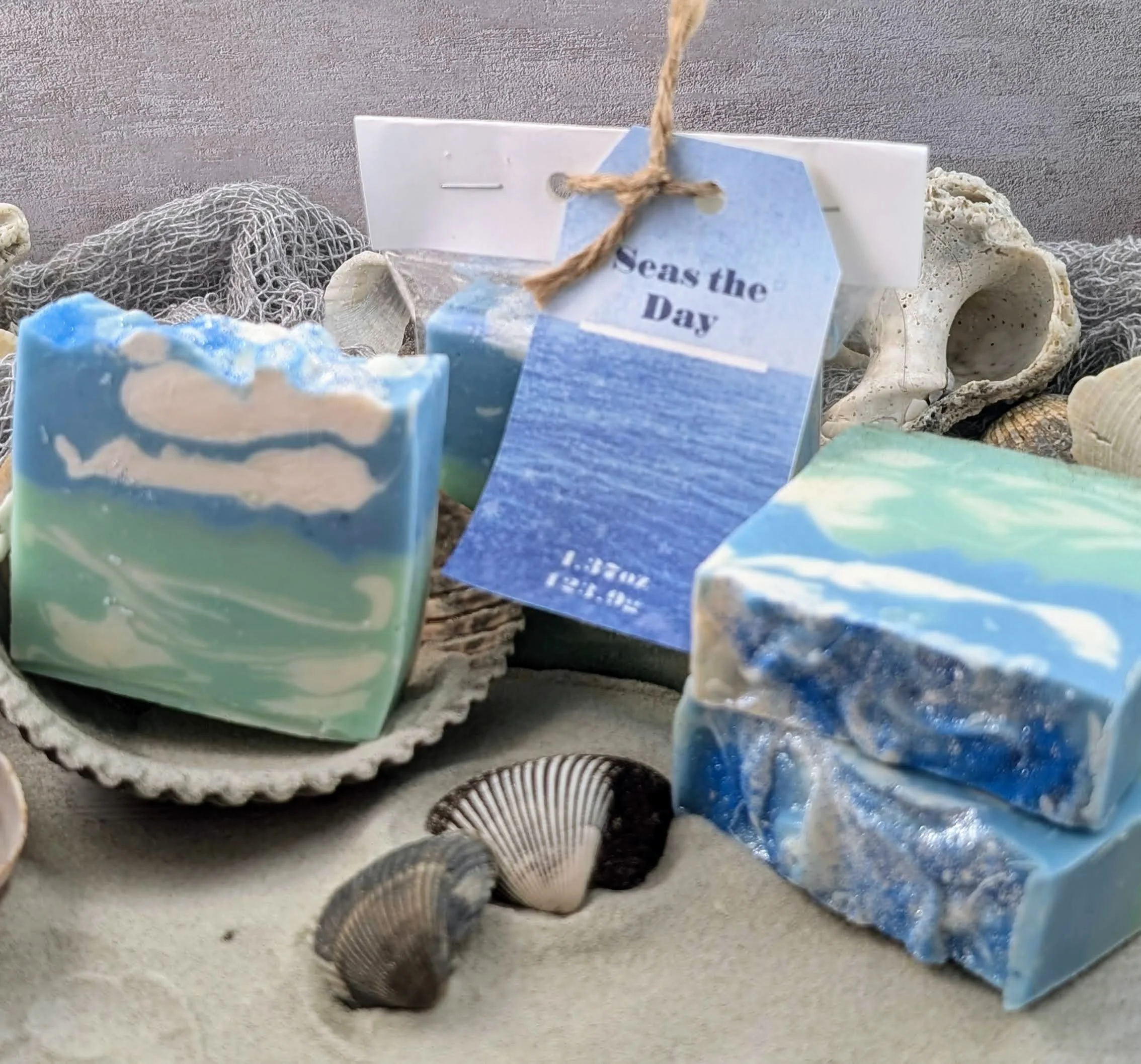 Assorted seashells and ocean-themed soap bars with a seashell and netting, and a tag reading 'Sea the Day'