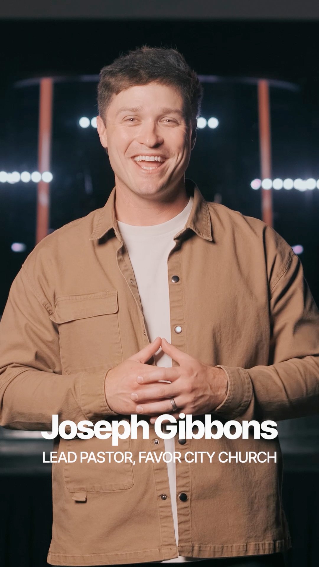 A smiling man in a beige jacket and white shirt standing in front of a dark background with bright lights. Text on the image reads: 'Joseph Gibbons, Lead Pastor, Favor City Church.'