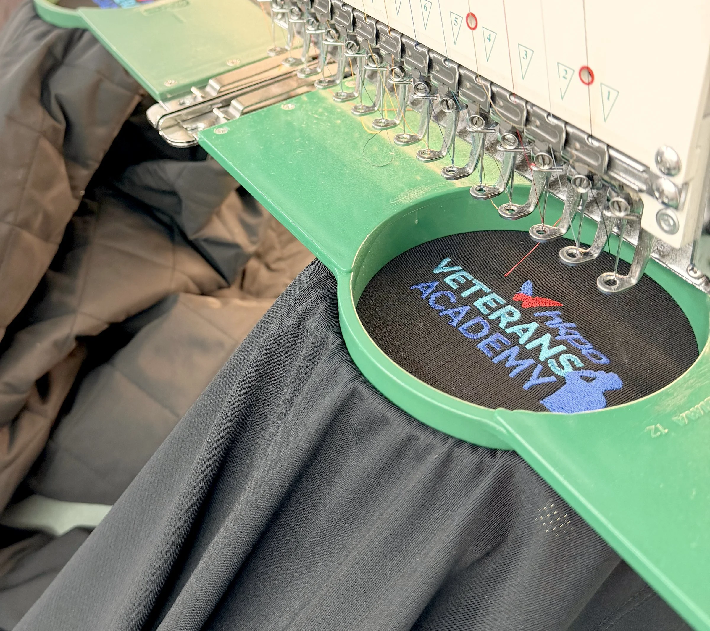 Veterans Academy logo being embroidered on a jacket on a multi-head machine at Uniforms & More