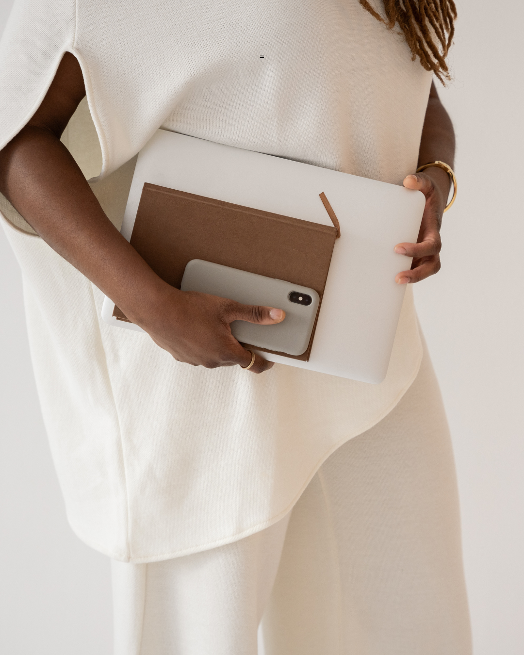 Person holding a laptop, notebook, and smartphone.