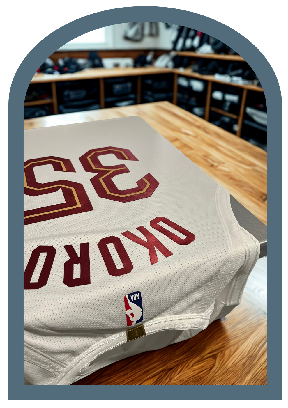 A white Cleveland Cavaliers basketball jersey with wine and gold trim, in a wooden table in a workroom.