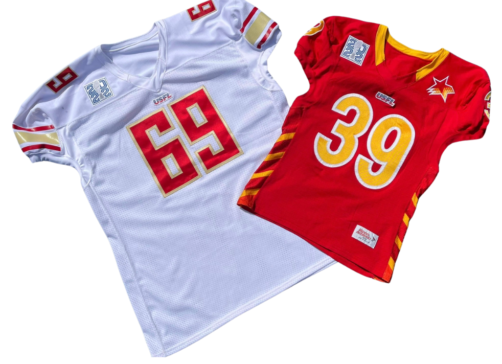 Two USFL football jerseys, one white with red and gold accents and the number 69, the other red with yellow and white accents and the number 39, laid flat on a surface.