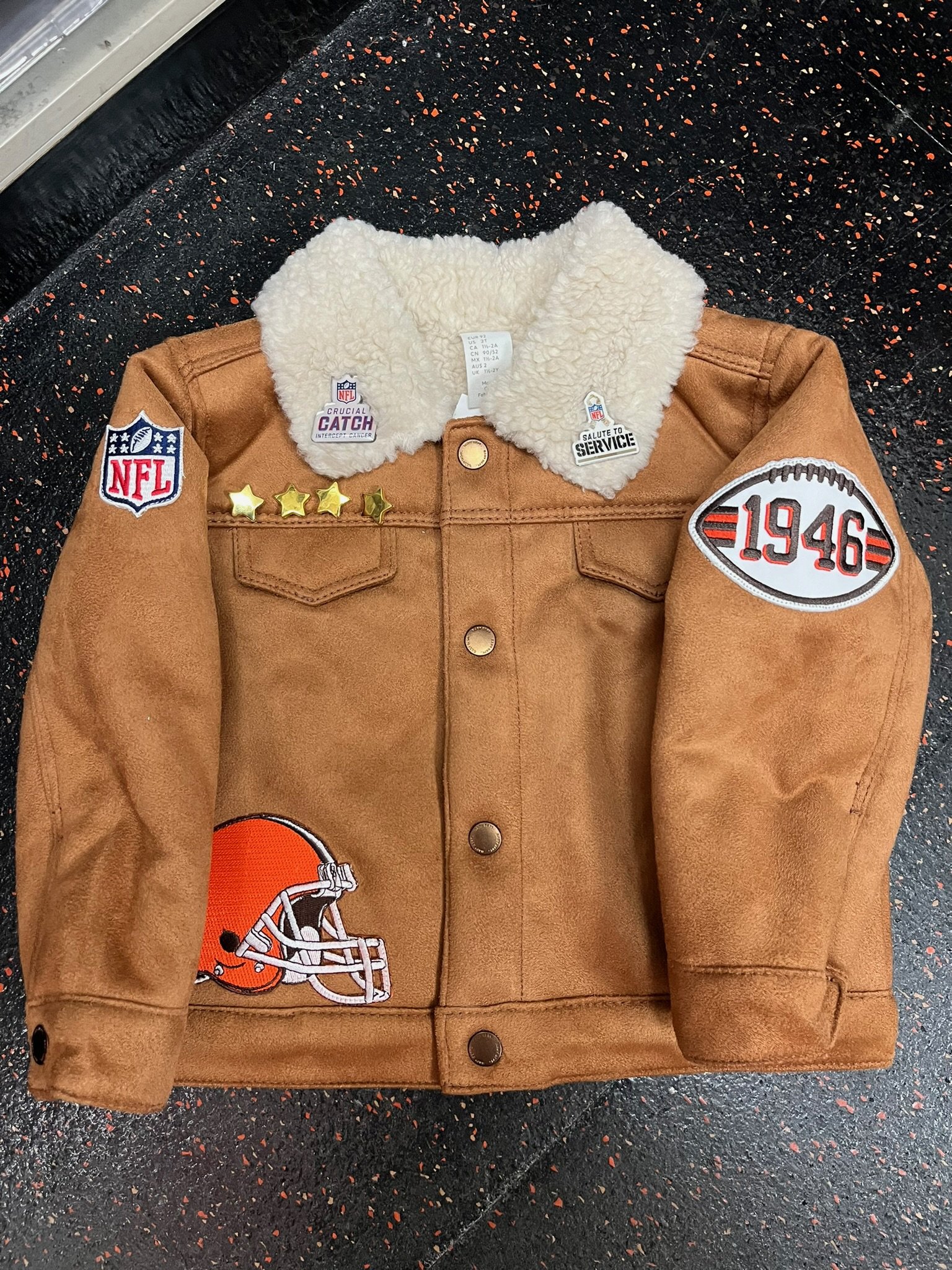 Cleveland Browns suede jacket with various football related patches on the front. The jacket has a beige shearling collar and metallic buttons.