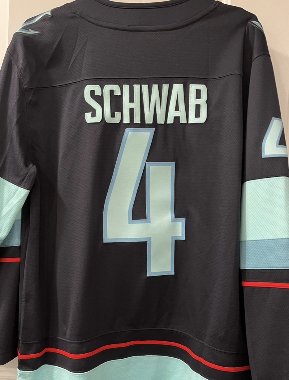Back of a black hockey jersey with light blue and white accents, the name 'SCHWAB' in white above a large number 4 with light blue and white outline.