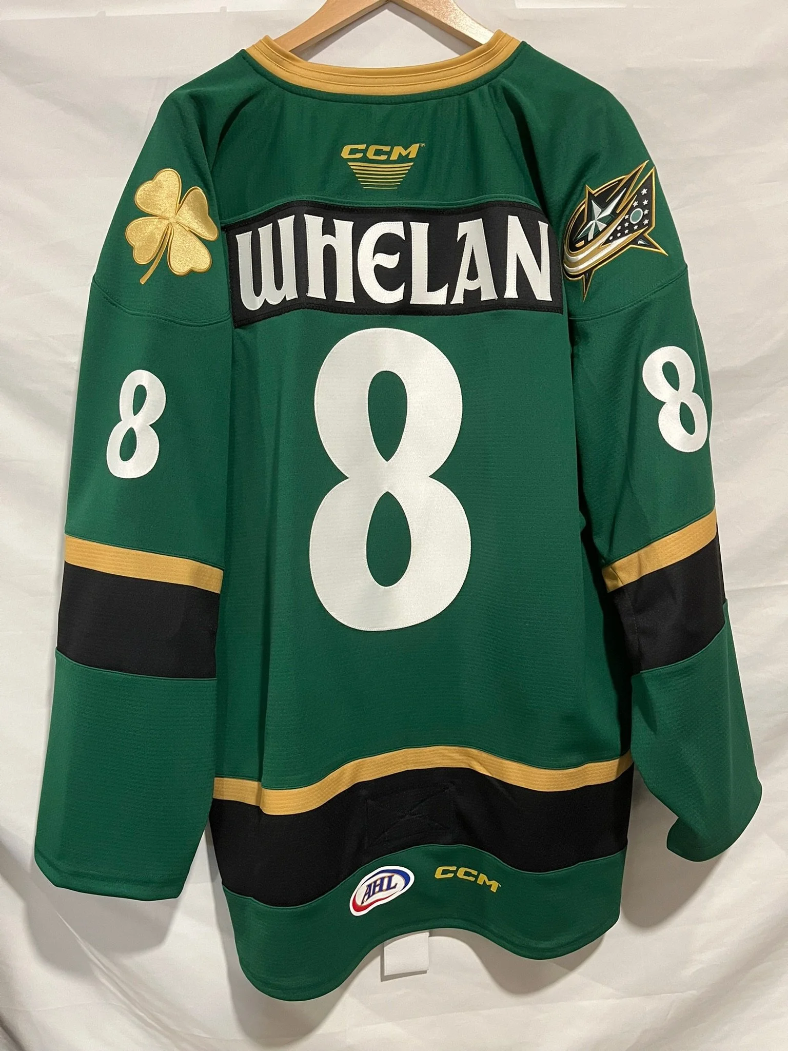 Gaelic St Patricks themed green hockey jersey with gold accents and logos, displayed on a hanger. It has the number 8 on the back, the name 'WHELAN,' and patches including the NHL logo, the CCM brand, and a clover leaf and star emblem on the sleeves.