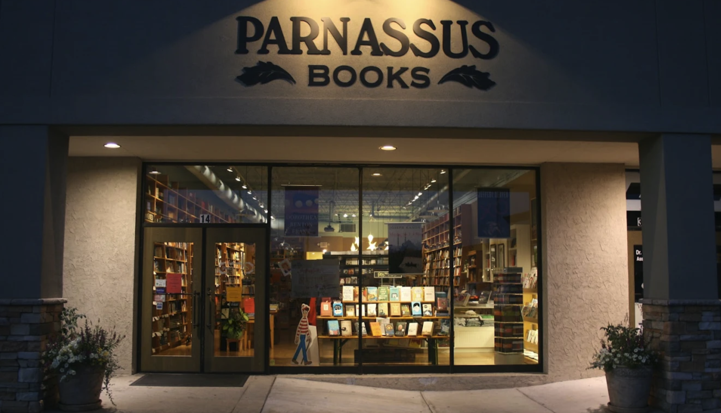 Front view of a bookstore called Parnassus Books, with large glass windows showing bookshelves inside and potted plants outside.