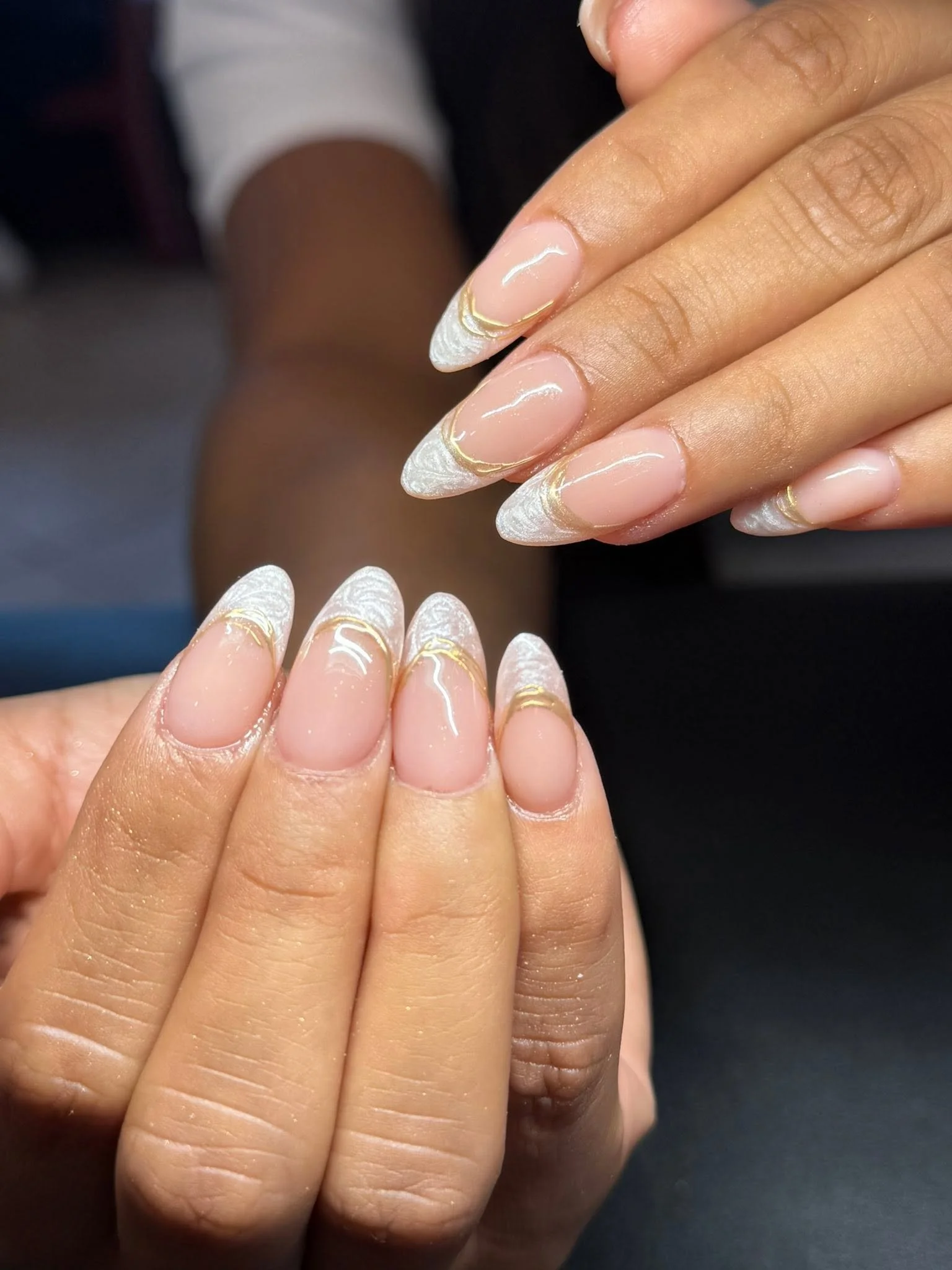 Close-up of a person's hand with manicure featuring a French tip design with white tips and gold accent lines.