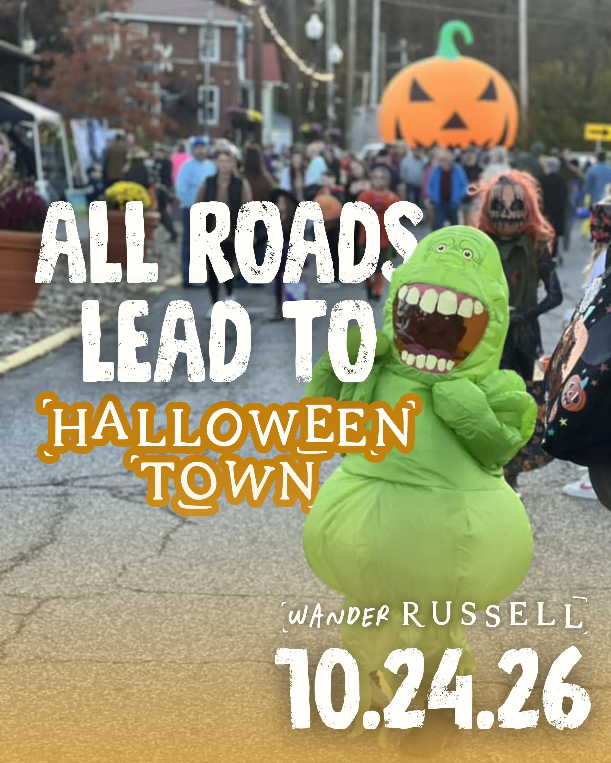 A person dressed in a bright green costume with a large open-mouthed monster face mask is participating in a Halloween parade on a street. The background features an orange pumpkin-shaped balloon, a crowd of people, and city houses.