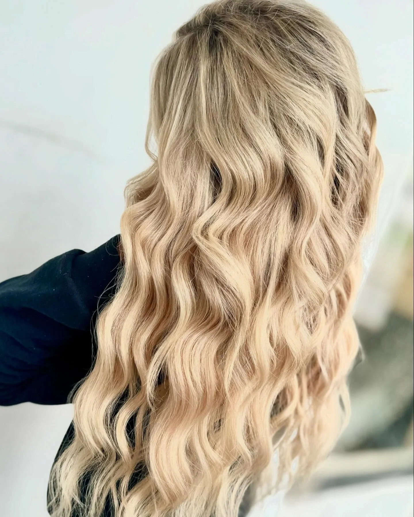 Close-up of blonde wavy hair with a soft curl pattern, smooth and shiny, seen from the back or side.