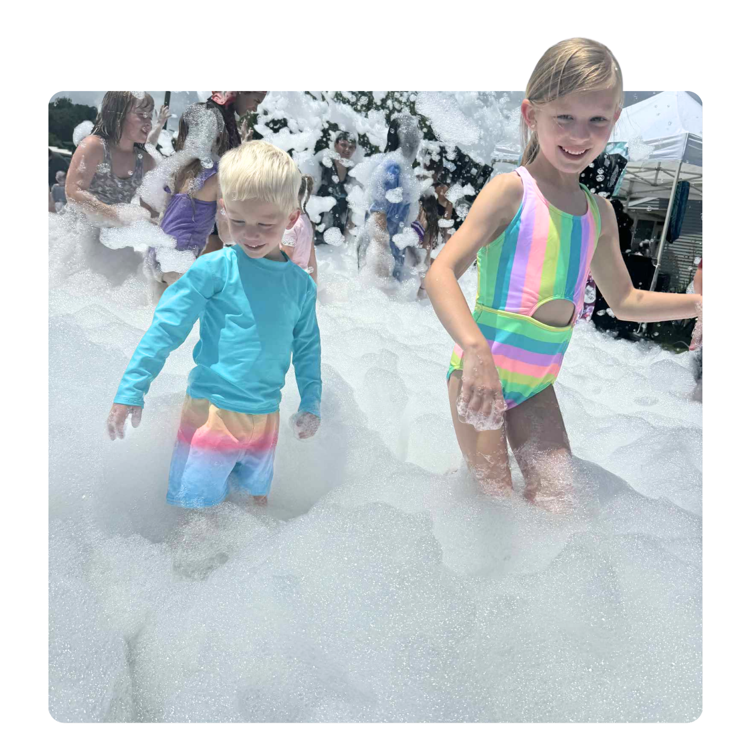 Children playing in foam at an outdoor event on a sunny day.