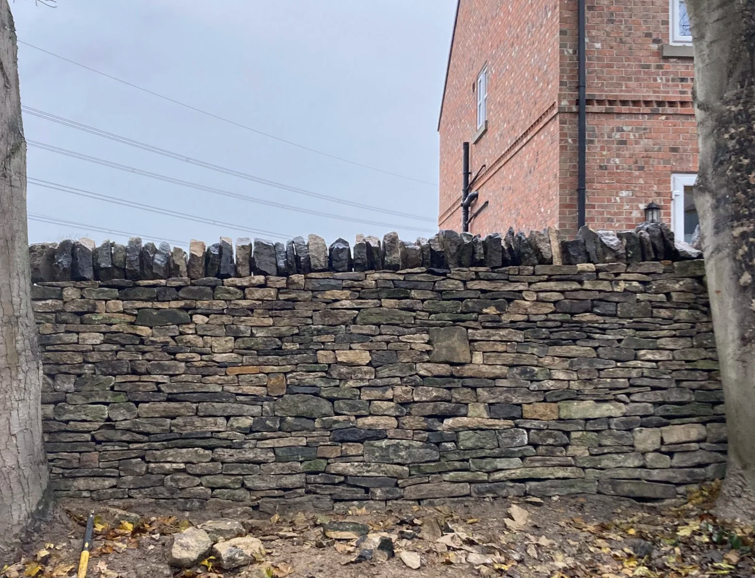 dry Stone wall with uneven, stacked stones in front of a brick building.
