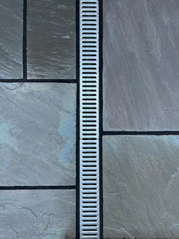 Close-up of a drain grate embedded in a tiled floor with grey and beige tiles.