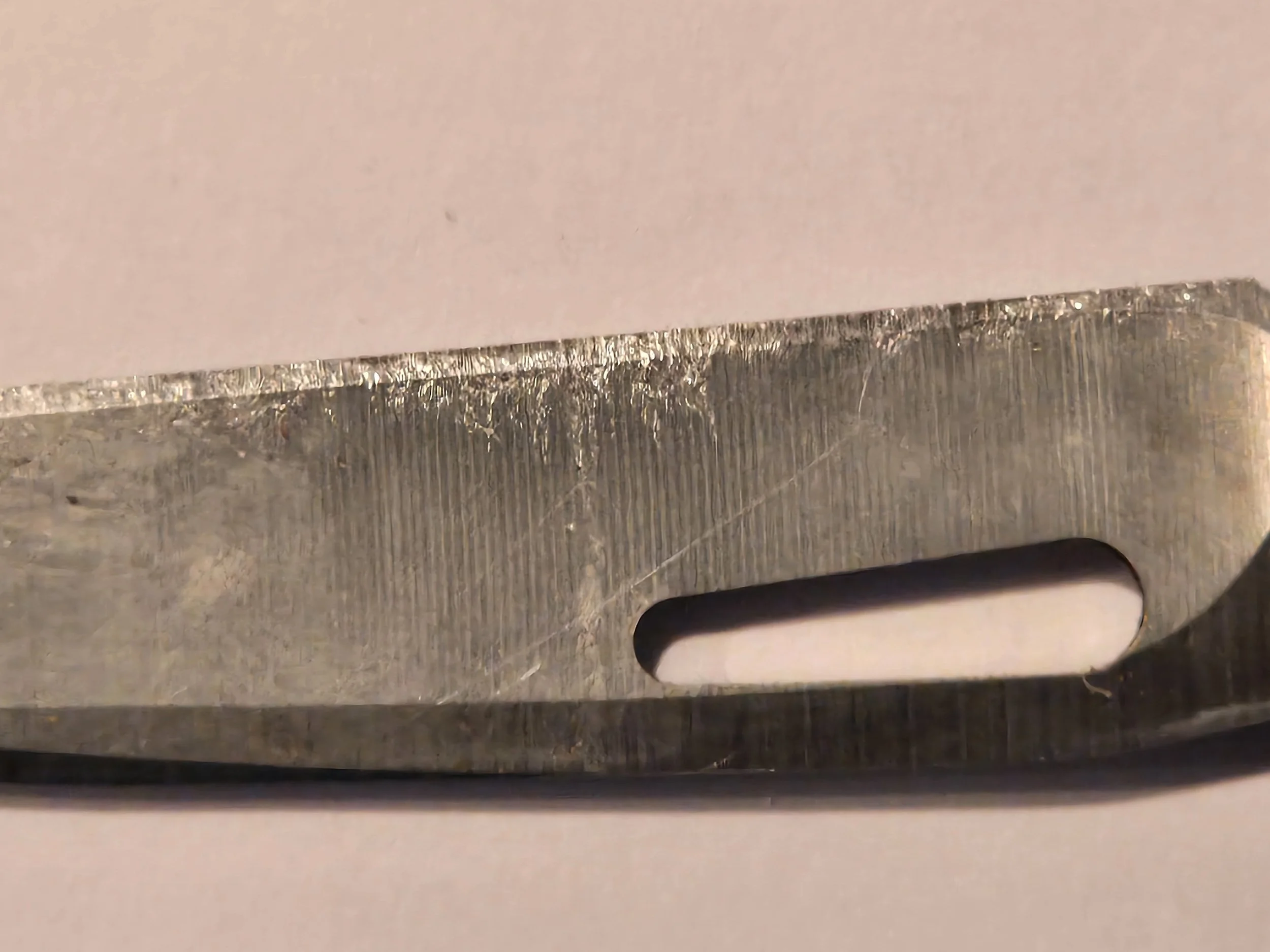 Close-up of a metal sewing machine needle with an elongated eye section.