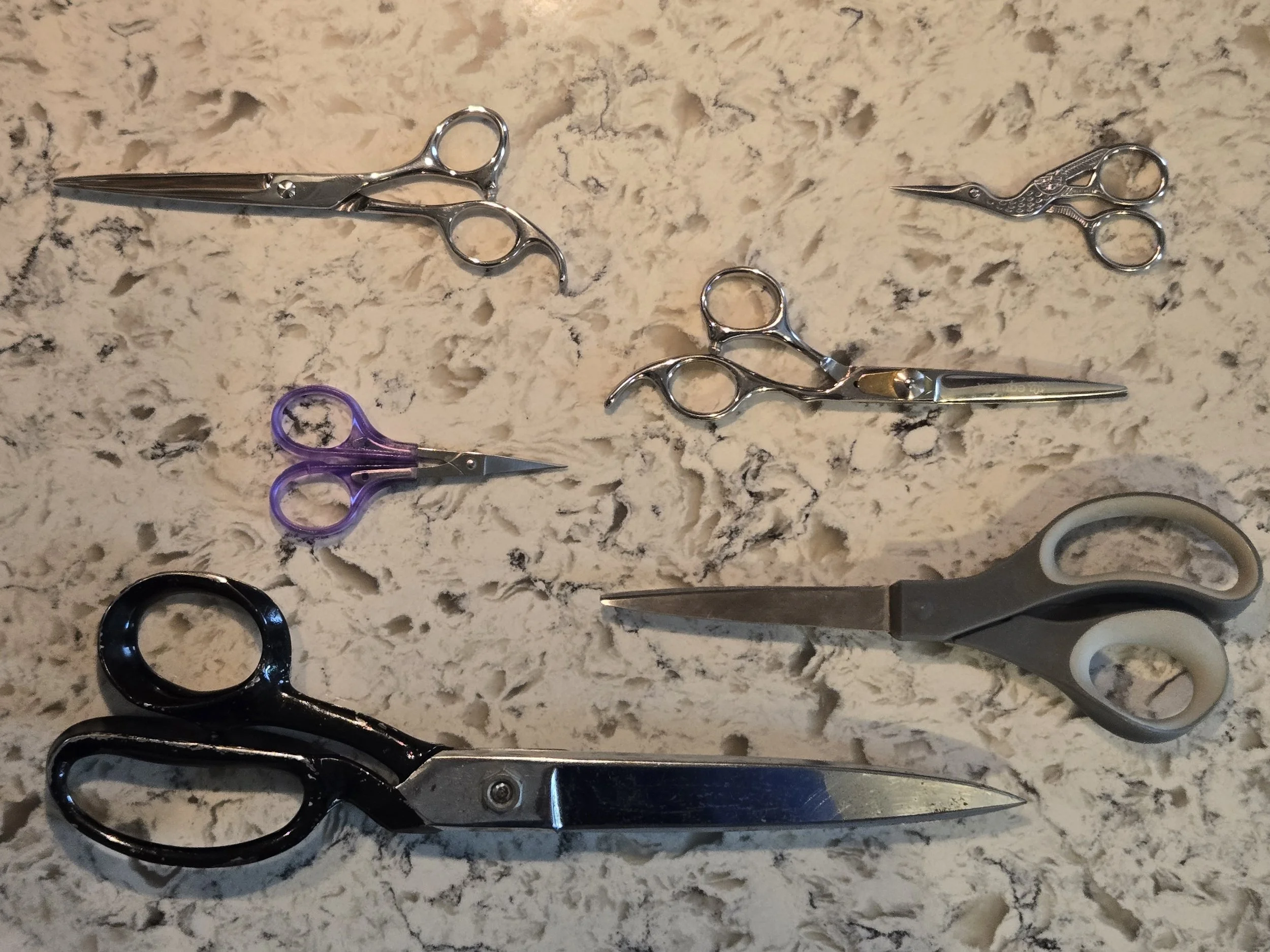 Six pairs of scissors of various sizes and designs laid out on a beige textured surface.
