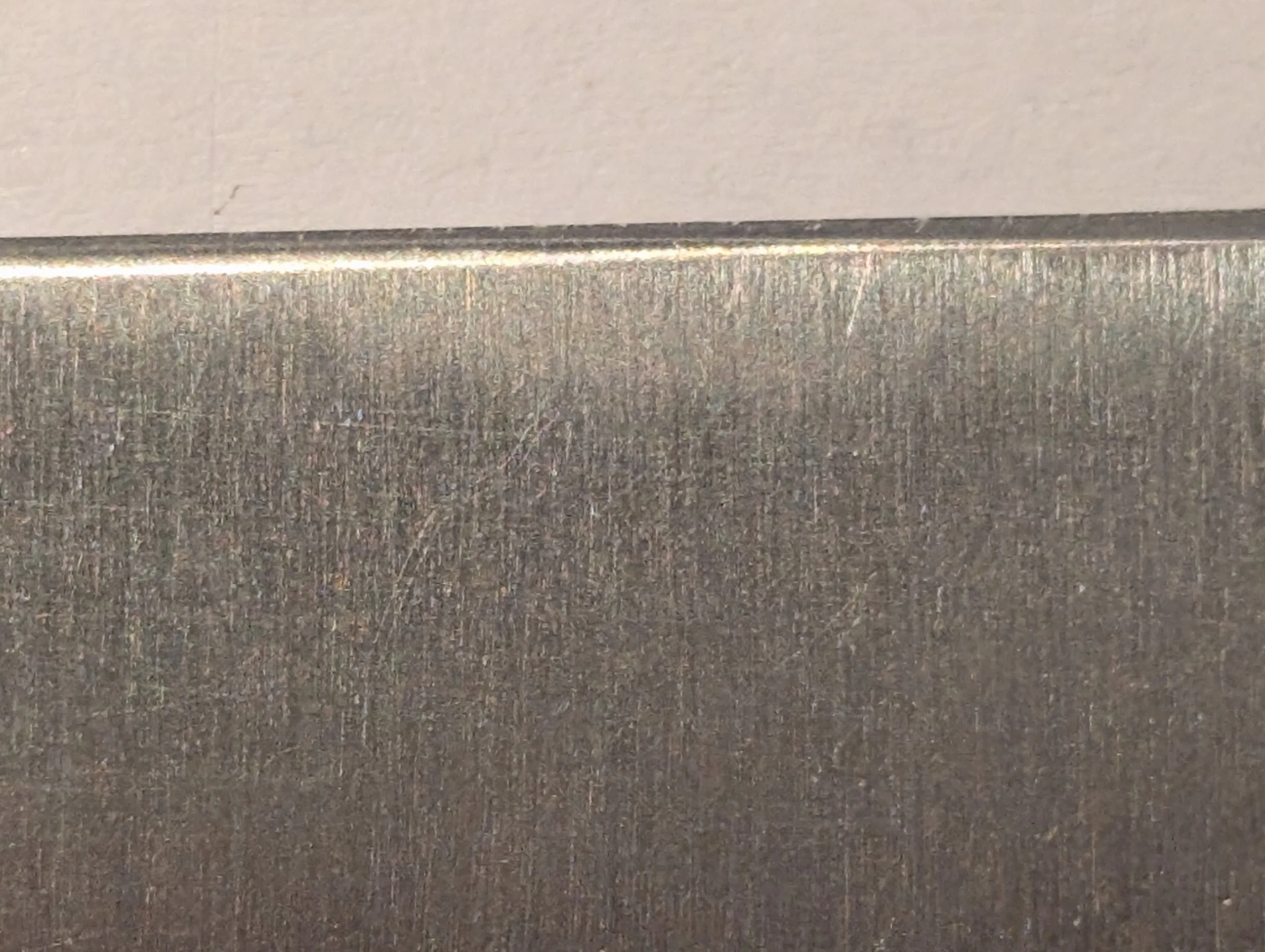 Close-up of a metal surface with visible texture and a smooth, shiny edge at the top.