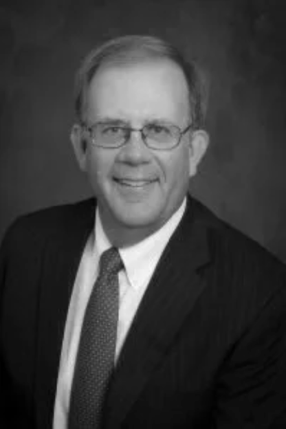Black and white portrait of a middle-aged man with glasses, wearing a suit and tie, smiling at the camera.