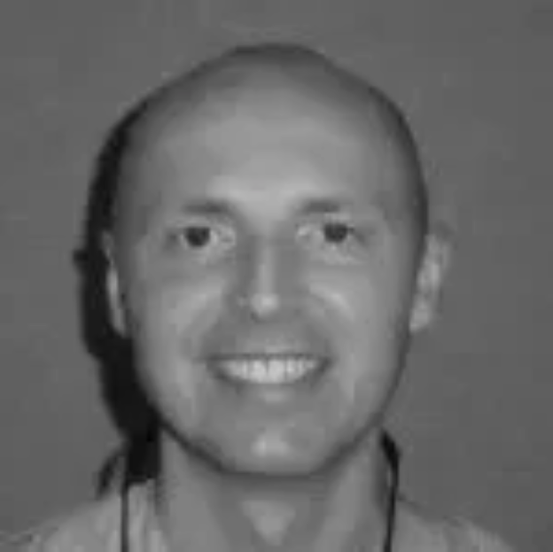 Black and white photo of a smiling man with short hair, wearing a light-colored shirt.