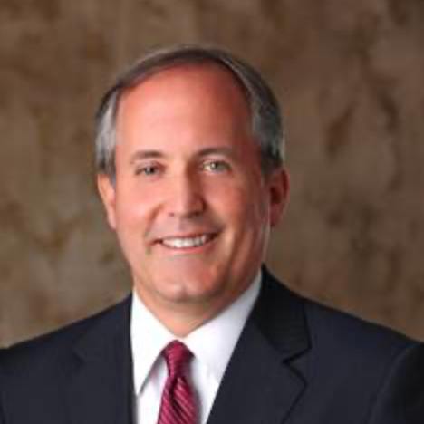 Portrait of a smiling middle-aged man in a dark suit with a white shirt and a red tie, against a textured brown background.