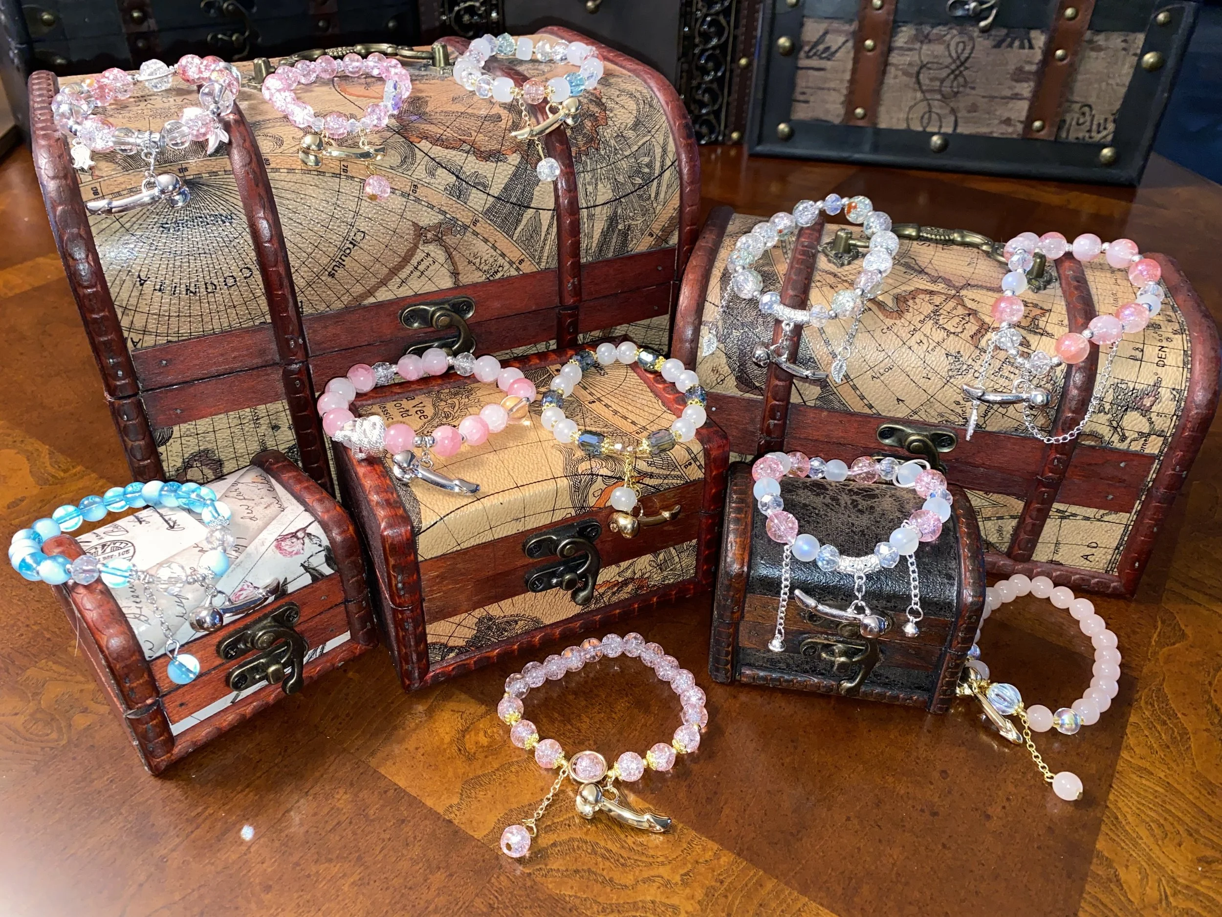 Multiple beaded bracelets and necklaces displayed on small vintage-style treasure chests, with a decorative map design on the chests.