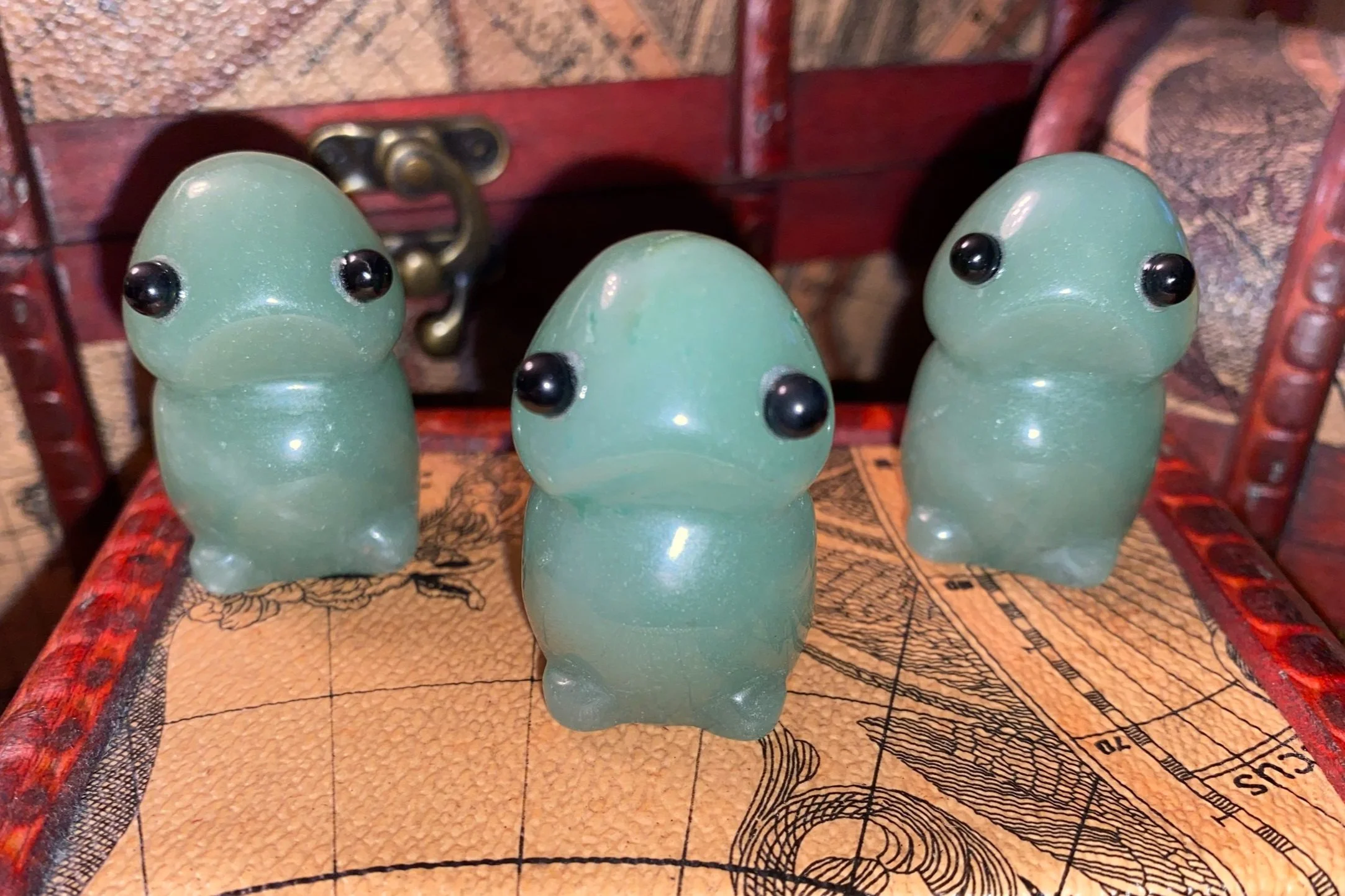Three green, cartoonish, snake-shaped figurines with black eyes are positioned on a patterned wooden surface.