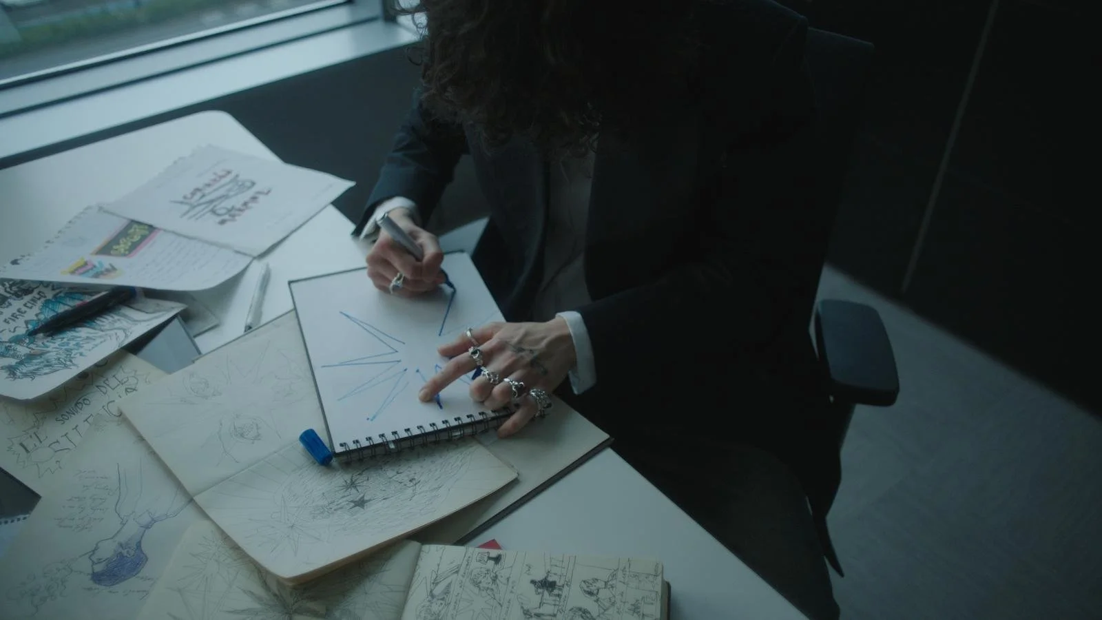 Alice Wonder Despierta videoclip Person sketching geometric shapes on a notepad at a desk with various doodles and sketches