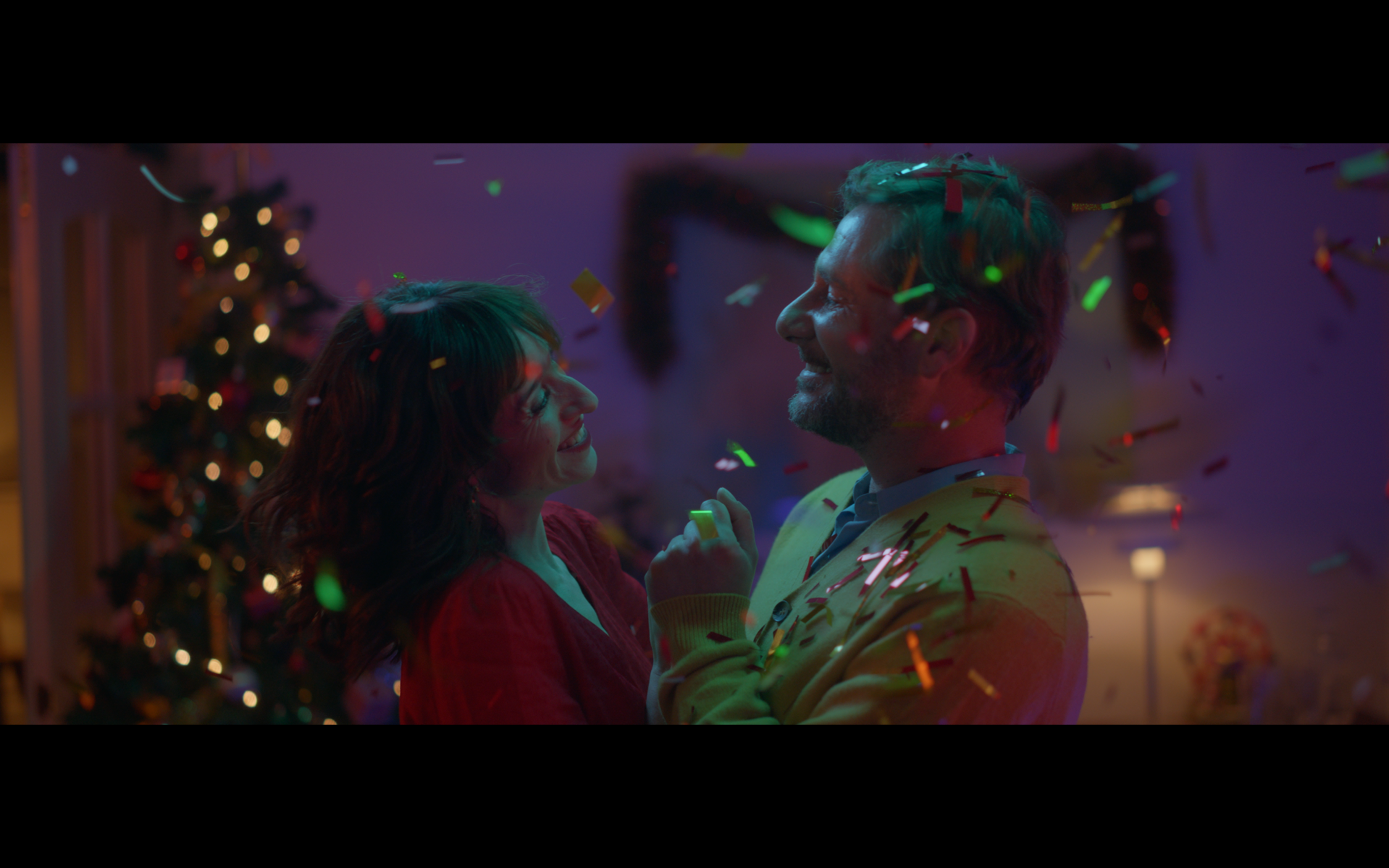 Mcdonalds spot A couple joyfully dancing surrounded by colorful confetti in a festive setting with a decorated Christmas tree in the background.