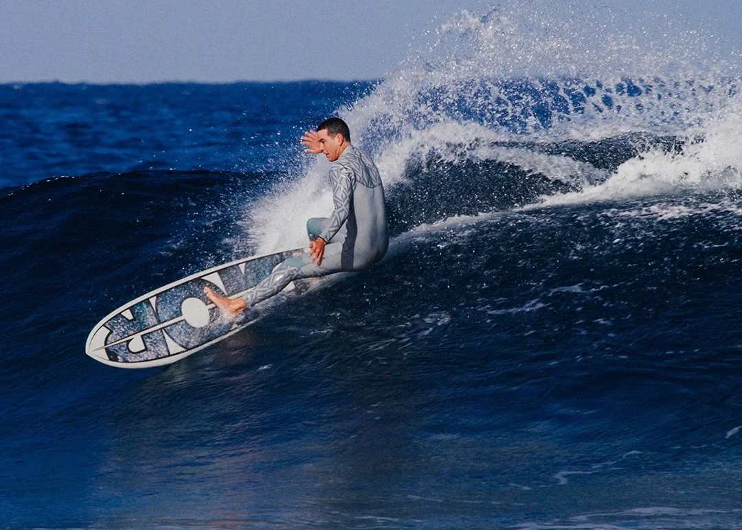 Dior Surf Tenerife Surfer riding a wave on the ocean in a wetsuit, performing a maneuver on a surfboard with spray in the air.
