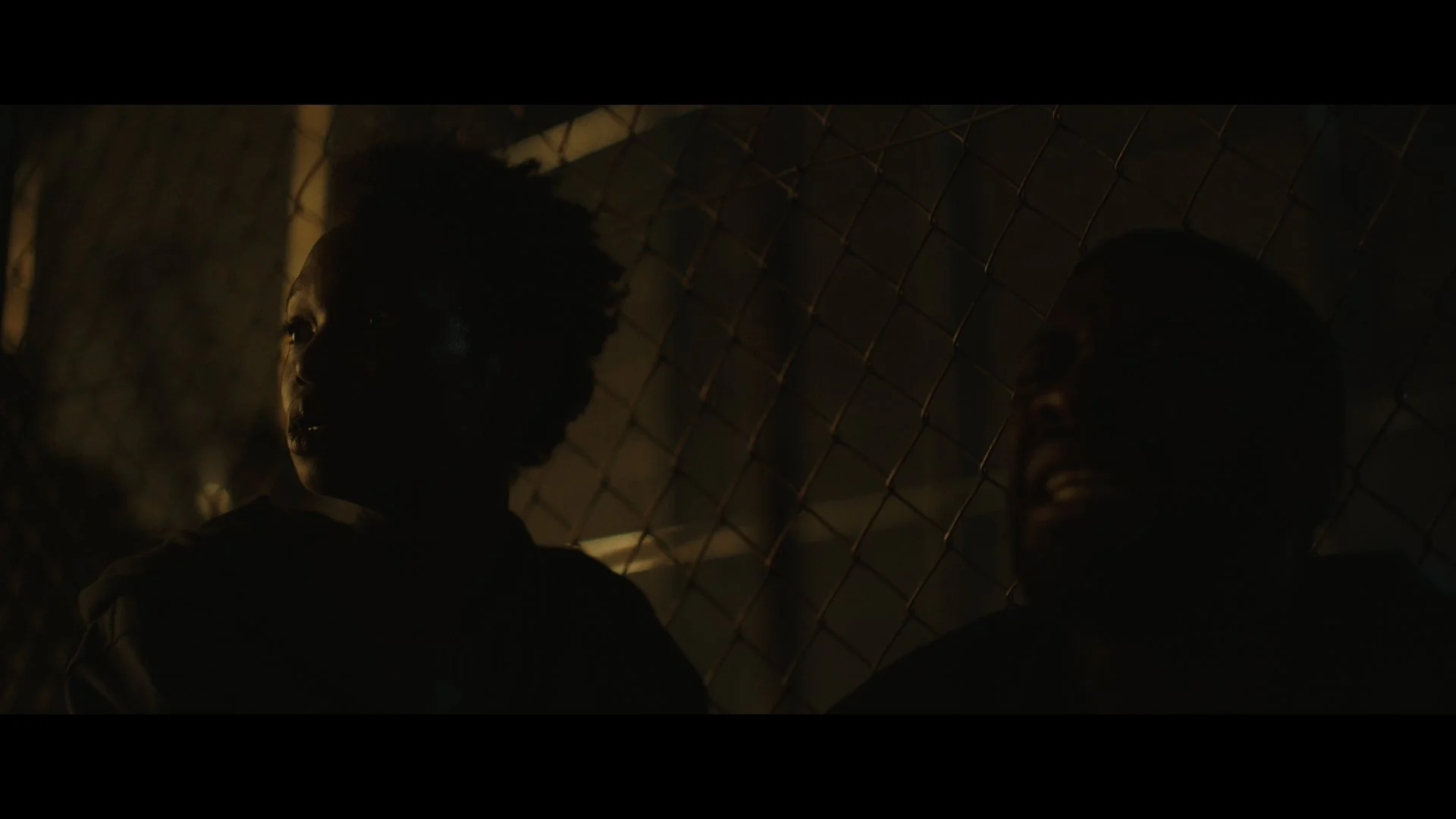 El Salto film Dark scene with two people in silhouette near a chain-link fence.
