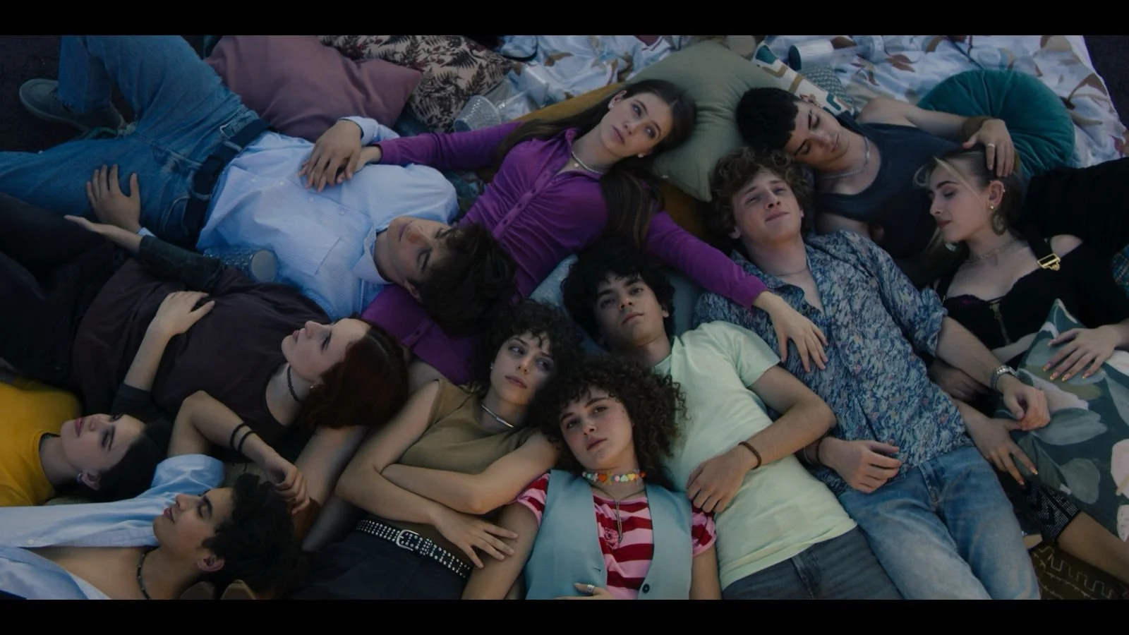 FOQ nueva generación - Group of young people lying on the ground with pillows, looking relaxed and close, in casual attire.