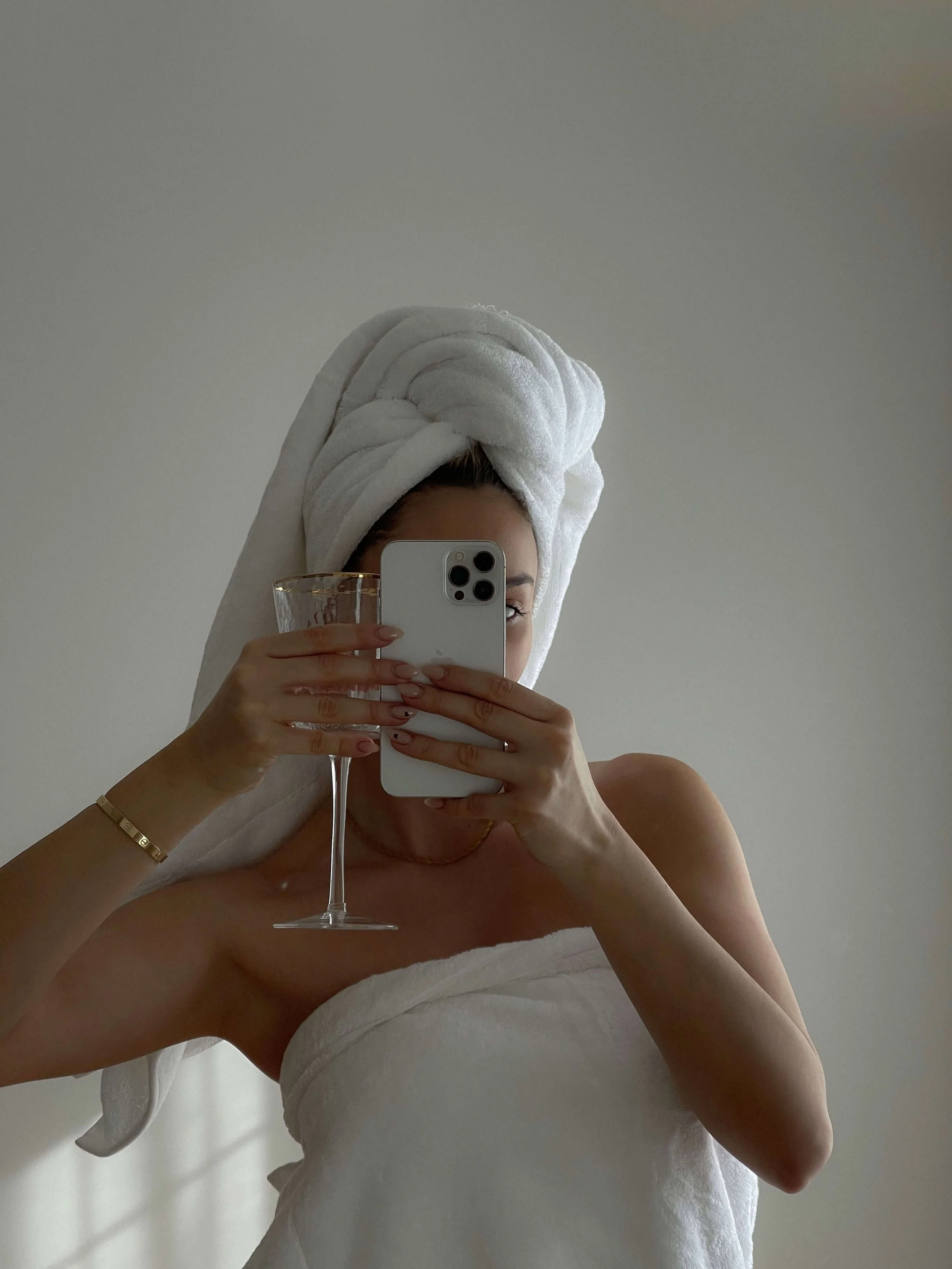 Woman wrapped iWoman wrapped in a towel with hair wrapped up, holding champagne—luxury self-care moment at Valos Hair Salon