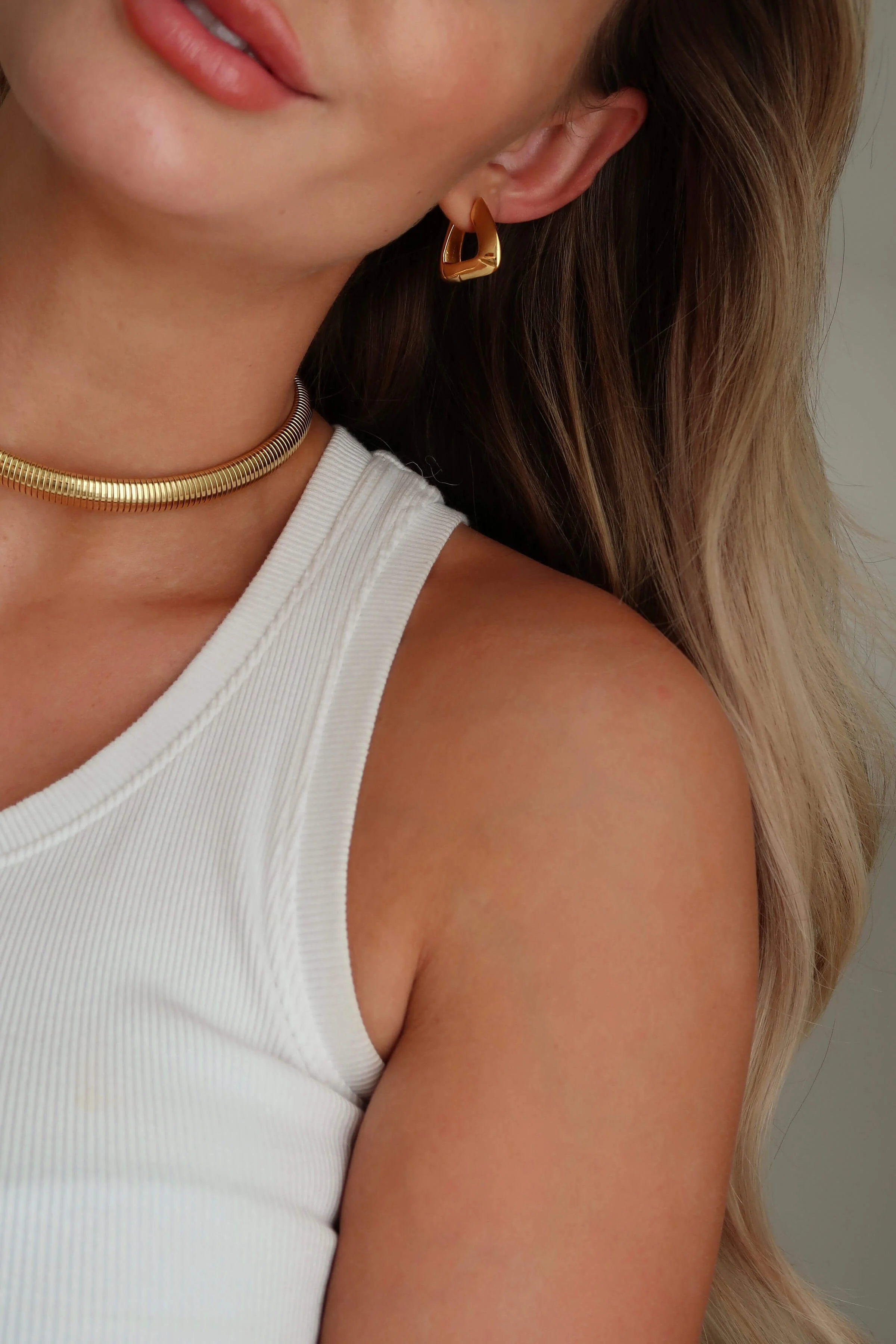 Woman with glossy, subtly waved hair and modern gold jewelry, capturing chic styling at Valos Hair Salon