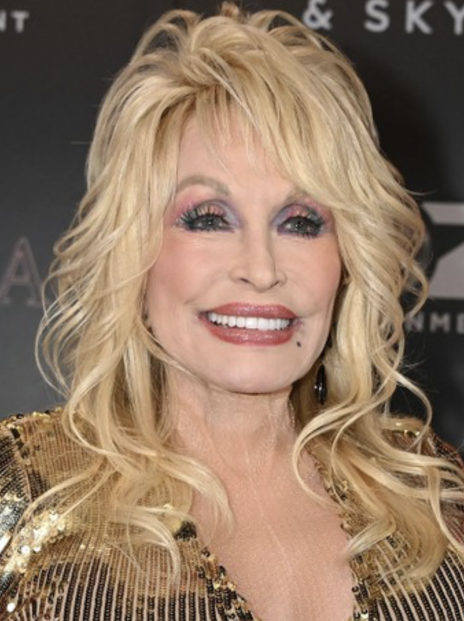 Dolly Parton smiles in a gold and black dress