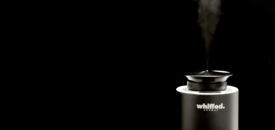 A black, matte aromatic diffuser emitting a thin plume of vapor in a dark environment.
