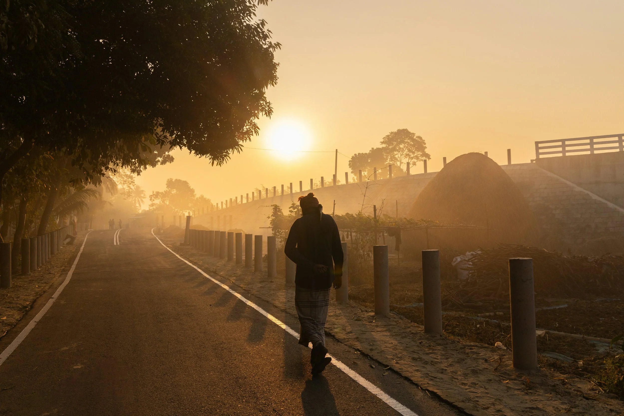 A lone figure walks along an empty road at sunrise, silhouetted against a warm golden mist