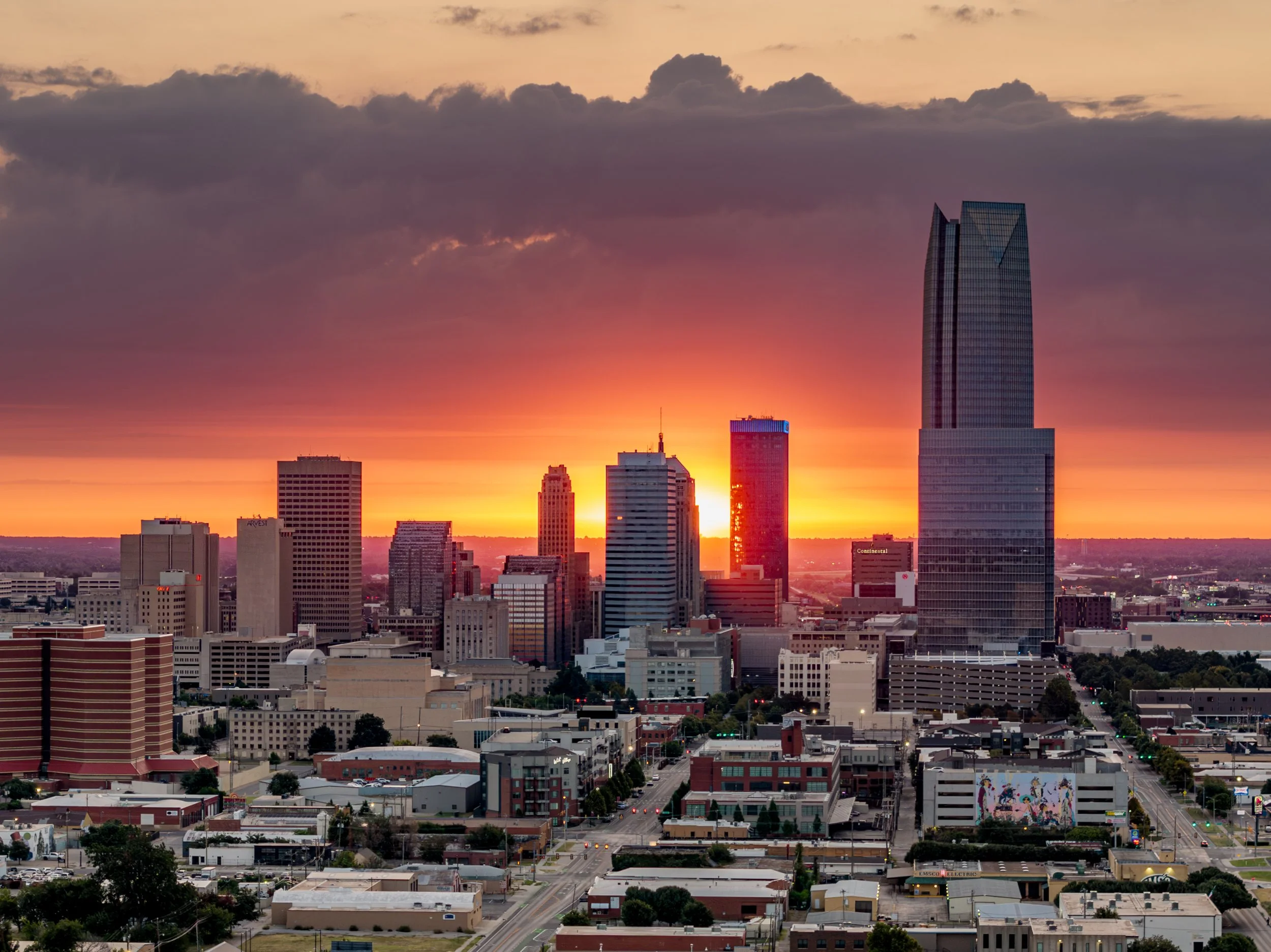Sunset over a city skyline with tall buildings and dark clouds in the sky.