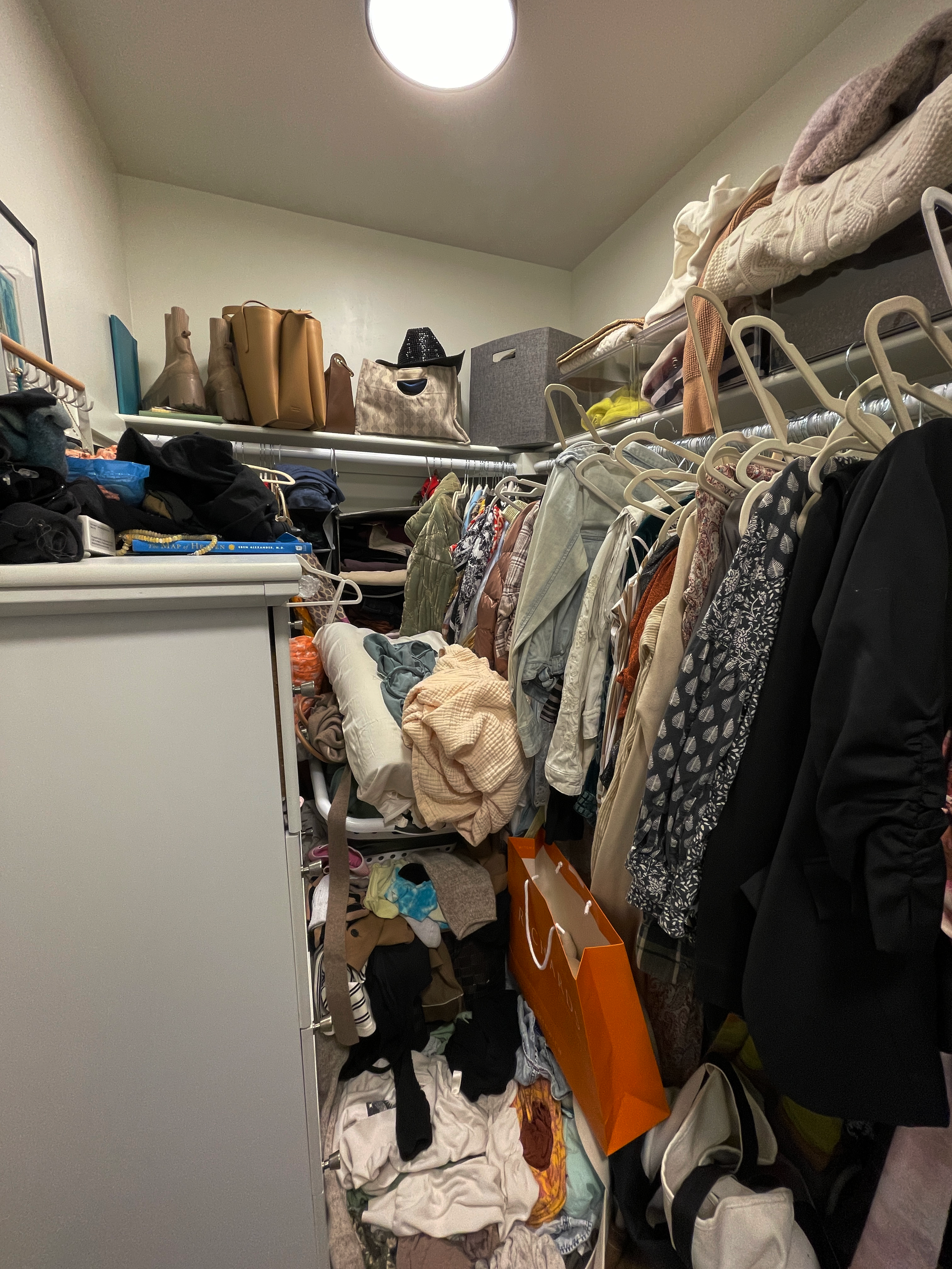 Before image of a small walk-in closet that is inaccessible due to a 3 foot high pile of clothing, with hangers askew and belongings disorganiezd.