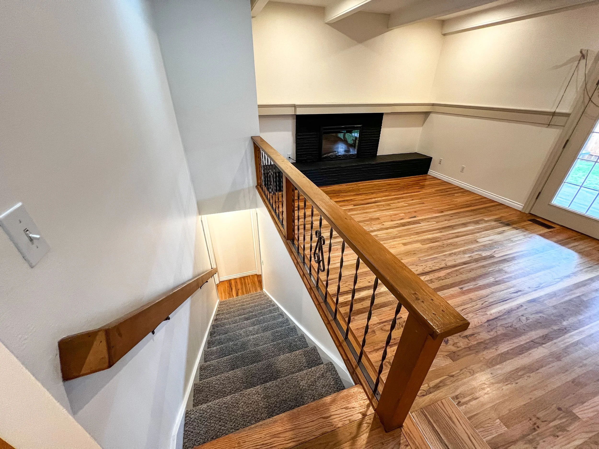 View of a staircase leading down to a living room with hardwood floors, a fireplace, and a glass door to an outdoor area.
