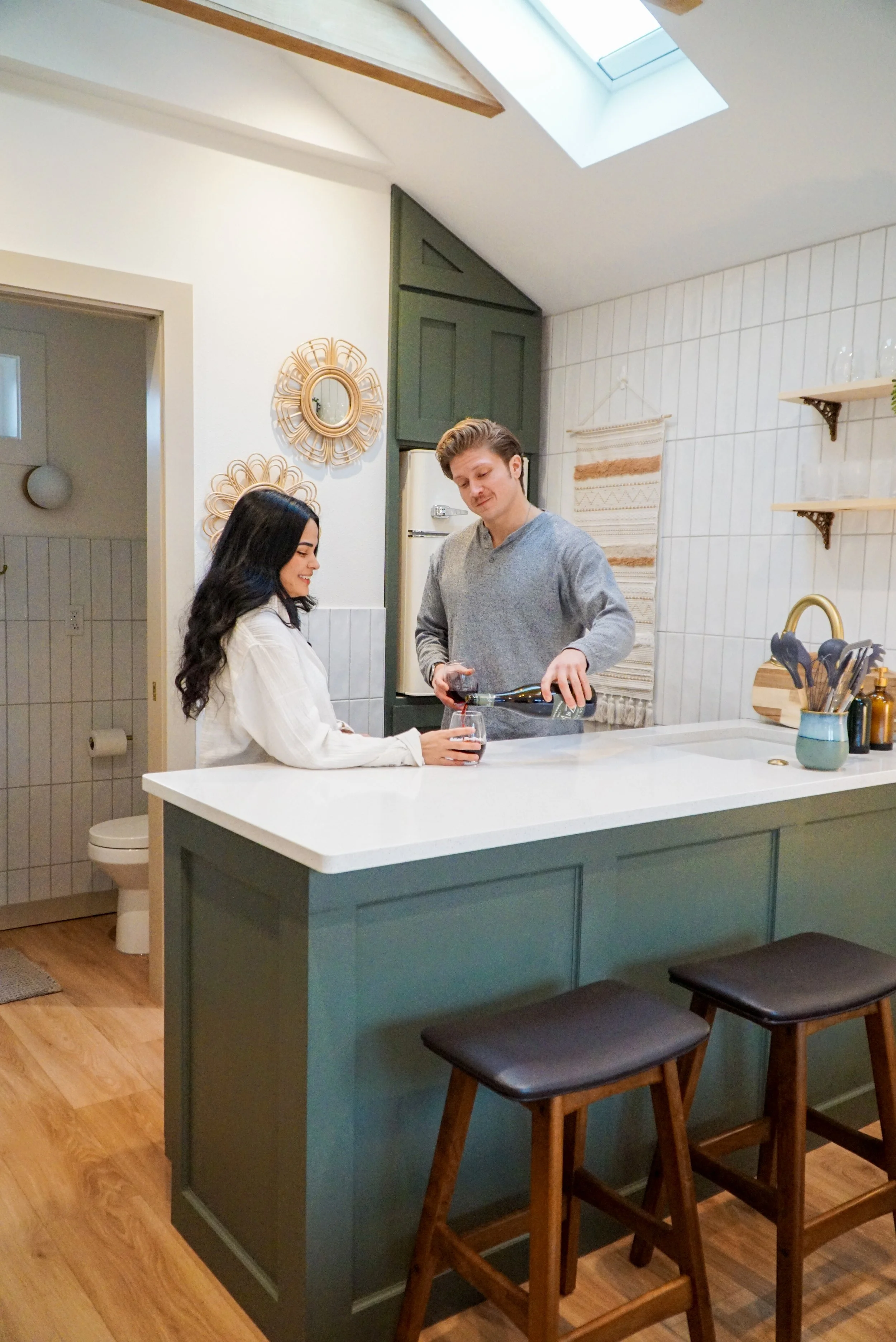 A man pouring red wine into a woman's glass at a kitchen island.