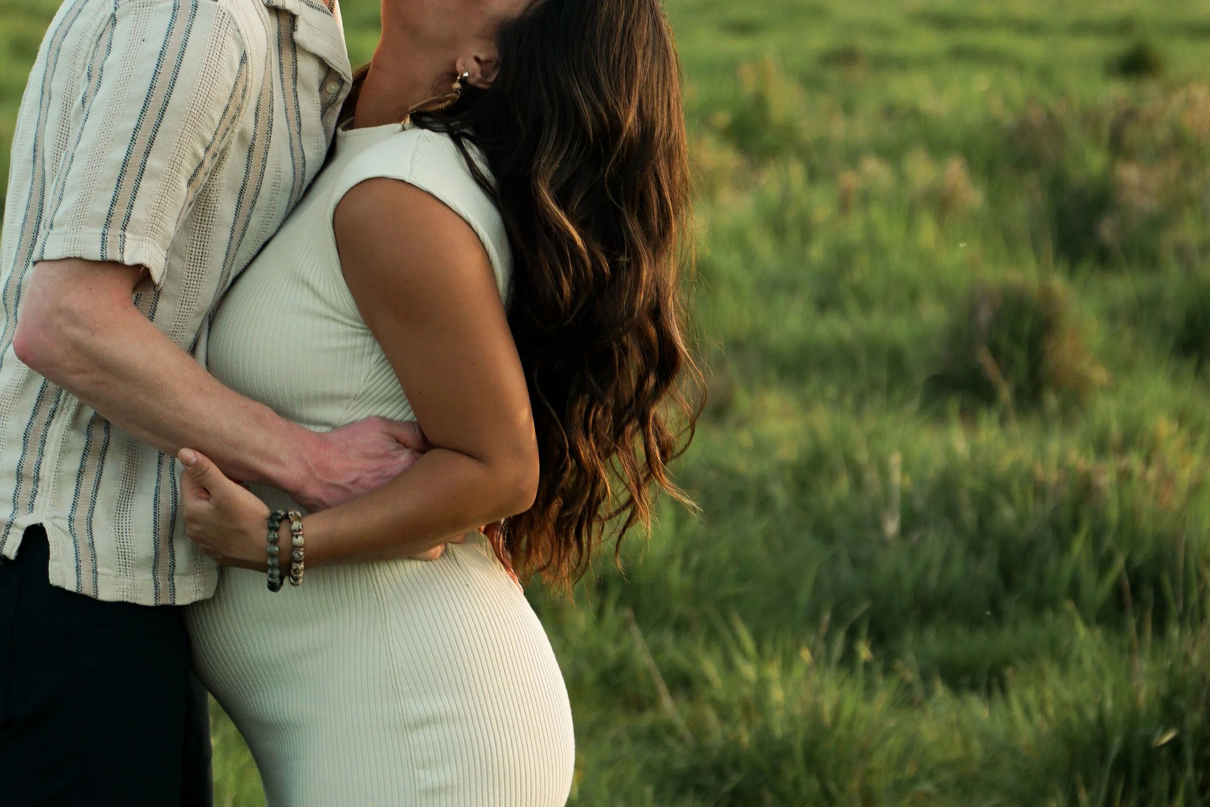 A couple embracing outdoors, with the woman's pregnant belly visible, in a grassy field.